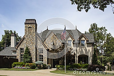 Rustic rock and brick upscale beautifully landscaped home with copper spires and chimney covers flying American flag on tall flagp Stock Photo