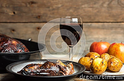 Rustic, romantic dinner - goose baked with apples and potatoes, next to a glass of red wine on a wooden background, rustic table Stock Photo