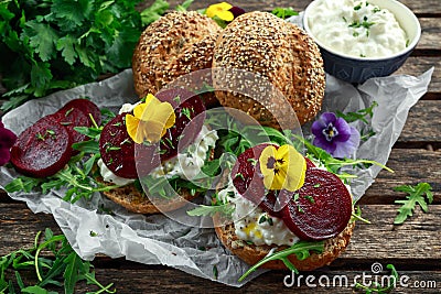 Rustic wholegrain buns with cottage cheese, rocket leaves, beetroot slices and edible viola flowers. Vegetarian food Stock Photo