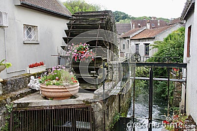 Rustic wooden waterwheel next to baskets of flowers with water flowing by. Crecy-la-Chapelle, France. Editorial Stock Photo