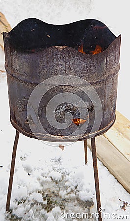 a rusty barrel with burning coals stands on the snow. Fire from a barrel. Stock Photo