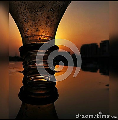 A rusty bottle reflection on water with a sunset creating a silhouette effect and shadows Stock Photo