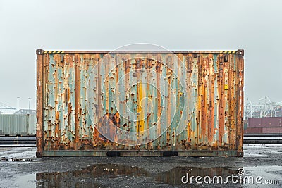 A rusty, dented shipping container battered by harsh weather, on a gloomy port background. AI generated. Stock Photo