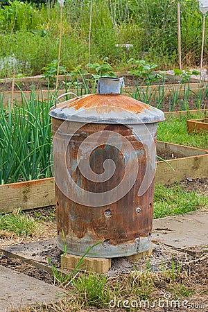 Rusty garden incinerator with plants in background Stock Photo
