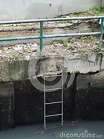 Rusty metal fence and ladder beside a dirty canal Stock Photo