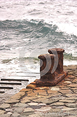 Rusty Noray with ocean waves in the background in a small harbor Stock Photo