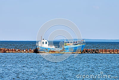 Rusty old abandoned fishing boat moored to rusty pier, wrecked weathered fishing trawler on sea Stock Photo