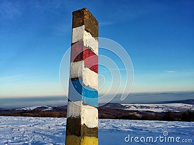 Rusty pole with touristic mark. Blue and red touristic direction sign. Path in winter hills with snow, blue clear sky Stock Photo