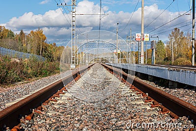 The rusty rails of the railway go into the distance in an autumn day, to the right is an empty platform. The photo is Stock Photo