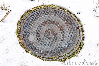 Rusty round storm drain manhole cover on snow covered grassy land in winter Stock Photo