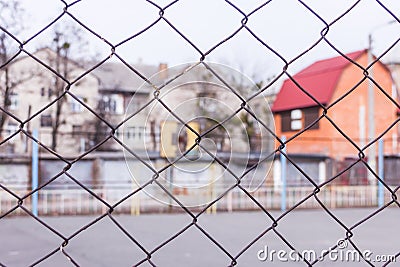 Rusty steel chain link or wire mesh as boundary wall. There is yard to the house with a red roof behind the mesh. Stock Photo