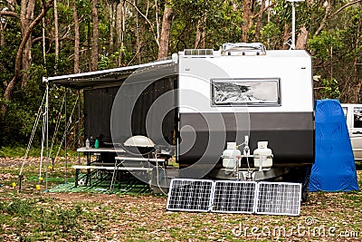 RV caravan camper on a campsite in the bush forest nature. Awning, portable toilet, solar panels, bbq, table. Family camping Stock Photo
