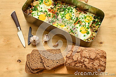 Rye bread, baked mixed vegetables and eggs close view, baking tray with tomatoes, broccoli and spices, home cooking Stock Photo