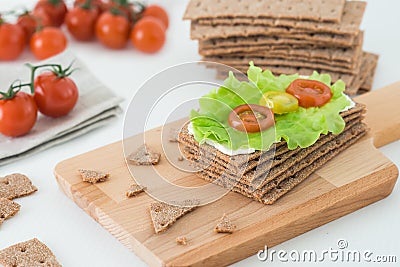 Rye crispy bread Swedish crackers with soft cheese, lettuce leave and cherry tomatoes on wooden board Stock Photo