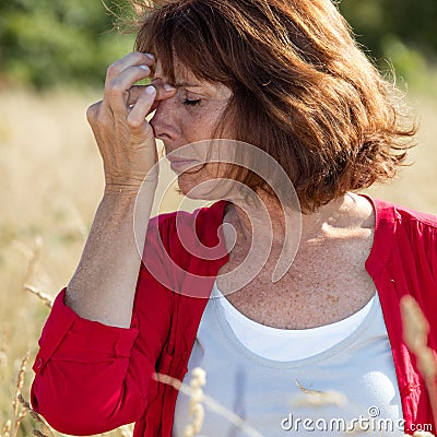 50s brunette woman massaging nose to soothe sinus pain outdoors Stock Photo