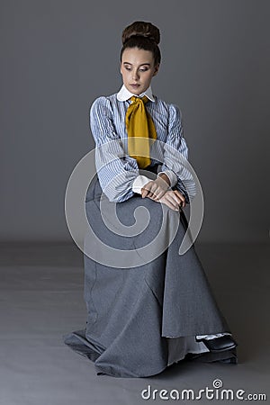 An Edwardian working class woman wearing a striped cotton blouse, mustard yellow cravat, and a grey walking skirt Stock Photo