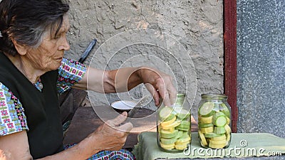 80s senior woman place fresh zucchini slices inside glass jars for homemade canning Stock Photo
