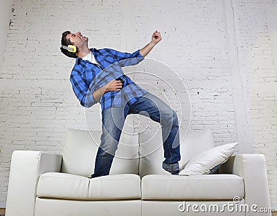 20s or 30s man jumped on couch listening to music on mobile phone with headphones playing air guitar Stock Photo