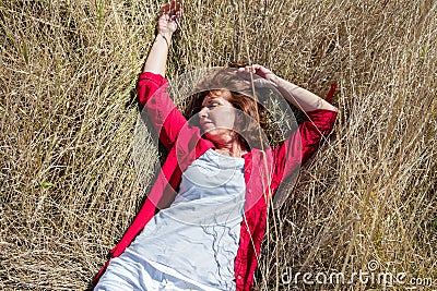 50s woman enjoying sun warmth sleeping peacefully on dry grass Stock Photo