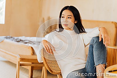 20s young teenage Asian woman wears a sweater looking away in stylish cozy room background. Attractive female model Stock Photo