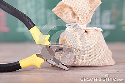 A sack of funds and a pair of pliers holding a Swiss franc in front of a blackboard with financial graphics Stock Photo