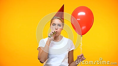 Sad adult woman blowing noisemaker holding balloon, bad mood at birthday party Stock Photo