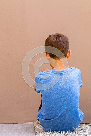 Sad alone boy sitting on the ground behind the wall outdoor Stock Photo