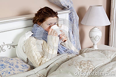 Sad alone young woman in white sweater and blue scarf feeling cold sick and resting home in bed. drinking her medicine drug and Stock Photo