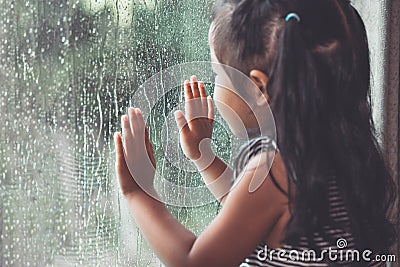 Sad asian little girl looking outside through the window Stock Photo