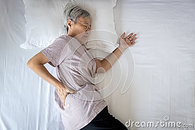 Sad asian senior woman touching hip on her bed,problem of pain while sleep feel backache discomfort,female old elderly suffering Stock Photo