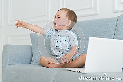 Sad baby crying near laptop - tantrum child on sofa Stock Photo