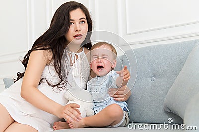 Sad baby crying near woman - tantrum child with mother on sofa Stock Photo