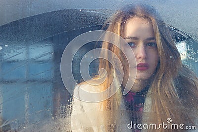 Sad beautiful seksalnaya Pretty sad lonely girl behind wet glass with big sad eyes in a coat Stock Photo