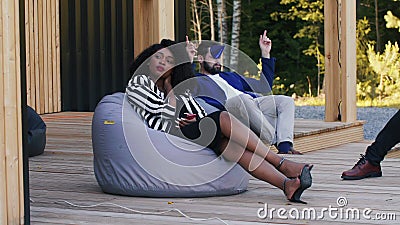 Sad birthday party. Beautiful young African woman is bored and lonely sitting on sunny terrace beanbag with friends. Stock Photo