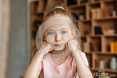 Sad bored pretty schoolgirl pupil studying at home, resting head on hand and looking at camera Stock Photo