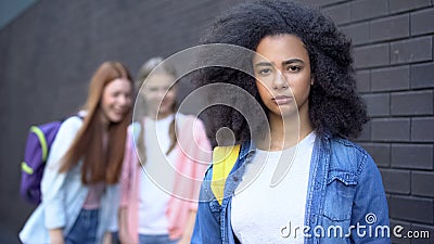 Sad bullying victim looking camera, female classmates teasing african schoolgirl Stock Photo