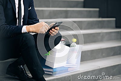Sad businessman sitting on stairs outdoor with box of personal stuff. Despaired male lost work place and looking for a Stock Photo