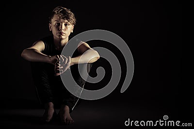 Sad child seated with arms around knees Stock Photo