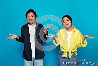 Sad confused millennial asian couple in casual spreads hands to sides, hold free space Stock Photo