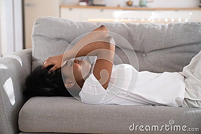 Sad depressed African woman lying on couch at home crying, feeling loneliness suffering from breakup Stock Photo