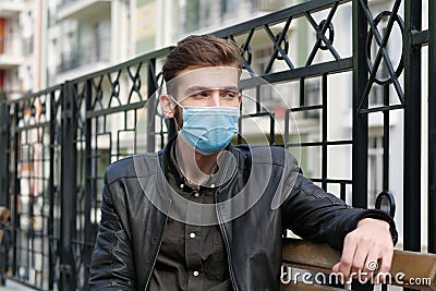 Sad depressed young man in medical protective face mask sits on the bench Stock Photo