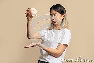 Sad and disappointed beautiful Asian woman holding a piggy bank with no money left Stock Photo