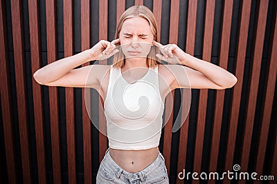 Sad and distracted girl is stnading at wall and closing her ears with fingers. Also she is keeping eyes closed. Isolated Stock Photo