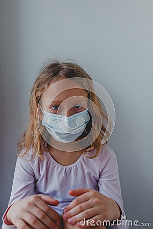 A sad European girl in a mask stayed at home during the quarantine and looks calmly at the camera Stock Photo