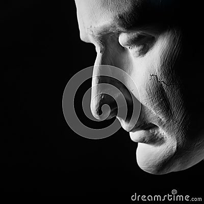 Sad face from plaster human head profile looking down and in strong contrast of light and shadow with simple dark black background Stock Photo