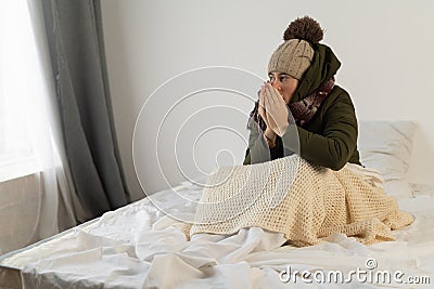 Sad female sit on bed at freezing cooled flat in warm cap and blanket shiver tremble with cold. Unhappy young woman at Stock Photo