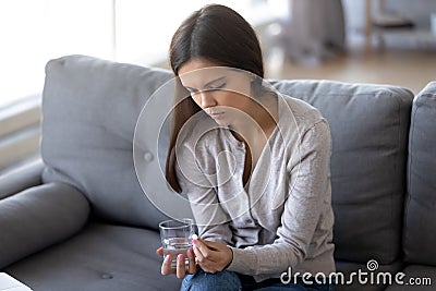 Sad female sitting indoors holding pill and glass of water Stock Photo