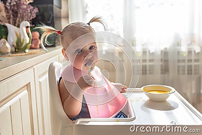 Sad funny naughty baby eating alone in the high chair Stock Photo