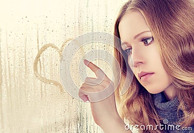 Sad girl draws a heart on the window in the rain Stock Photo