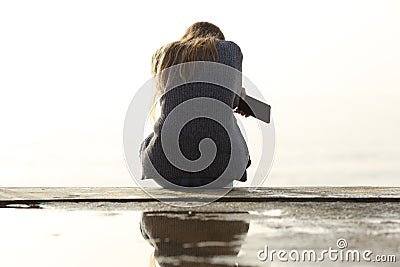 Sad girl holding phone complaining sitting on a ledge Stock Photo